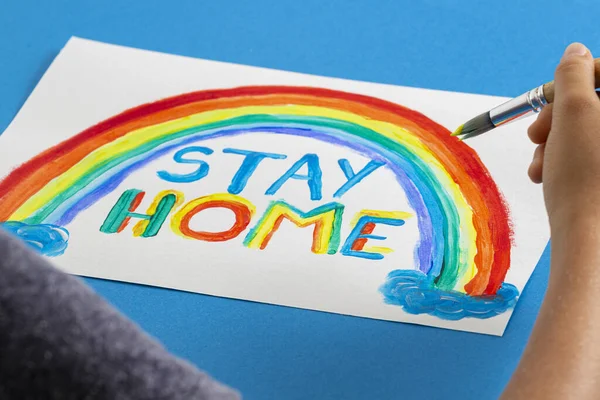 Pintura infantil durante la cuarentena en casa. Arco iris con palabras Quédate en casa. Campaña de medios sociales para la prevención del coronavirus — Foto de Stock