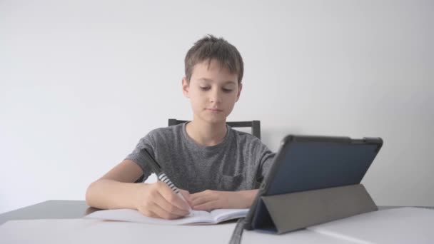 Online μάθηση, εξ αποστάσεως μάθημα, εκπαίδευση στο σπίτι, τεχνολογία για τα παιδιά. Αγόρι με διδακτικά βιβλία που κάνει σχολική εργασία και χρησιμοποιώντας ψηφιακό υπολογιστή tablet στο σπίτι — Αρχείο Βίντεο