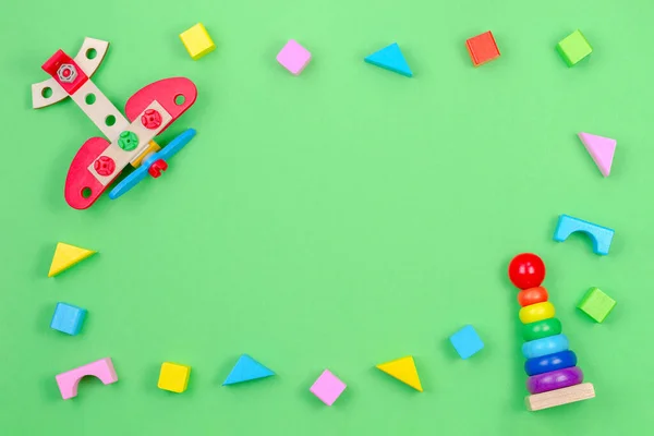 Дитячі іграшки фонова рамка з дерев'яною площиною, піраміда для укладання дитячих кілець та барвисті блоки на зеленому фоні — стокове фото
