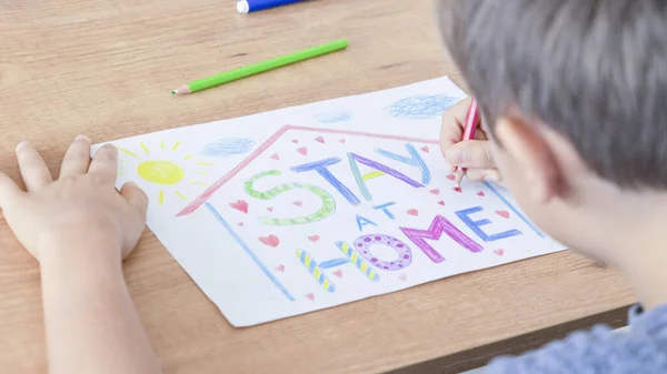 Παιδική ζωγραφική με χρωματιστά μολύβια κατά τη διάρκεια καραντίνας στο σπίτι. Μήνυμα εγγραφής Μείνετε στο σπίτι. Εκστρατεία μέσων κοινωνικής δικτύωσης για την πρόληψη του ιού coronavirus — Φωτογραφία Αρχείου