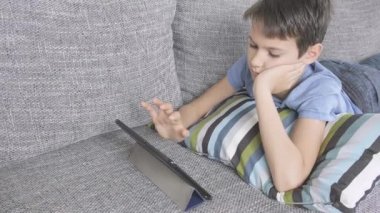 Evdeki dijital tablet bilgisayarla kanepede yatan çocuk. Teknoloji, uzaklık eğitimi, çevrimiçi öğrenme, oyun konsepti