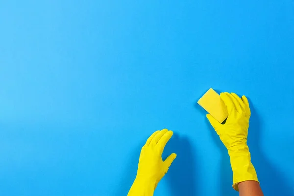 Mãos em luvas amarelas com esponja sobre fundo azul. Limpeza, desinfecção de casa — Fotografia de Stock