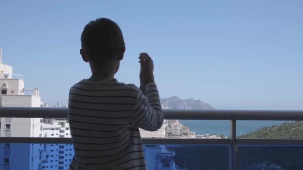 Ребенок аплодирует медицинскому персоналу с балкона. Люди в Испании хлопают по балконам и окнам в поддержку медицинских работников во время пандемии коронавируса — стоковое видео