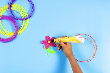 Mavi arkaplanda plastik filamanlı 3D kalemle çocuk eli oluşturma