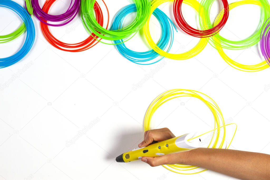Kid hand with 3d pen and colourful plastic filament on white table background. Top view
