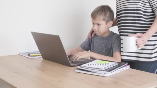 Aprendizaje infantil con computadora portátil, haciendo tareas en casa. Mamá vino a apoyarlo. Tecnología, educación a distancia, aprendizaje en línea desde el hogar — Vídeo de stock