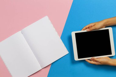 Dijital tablet bilgisayarı olan çocuk elleri ve açık mavi ve pembe arkaplan üzerine kağıt defter. Üst görünüm