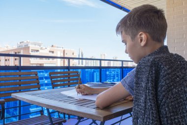 Çocuk yazarlığı, balkonda ödev yapmak. Okul, çevrimiçi öğrenim, uzaktan eğitim, evde eğitim, evde kalma kavramı