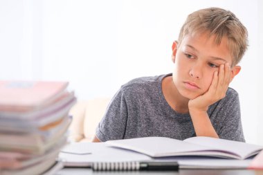 Öğrenci çocuk kitap yığınlarının arasında oturuyor, ders kitapları, çalışma kitapları masasında ve ödevlerini yapıyor. Eğitim, çevrimiçi öğrenme, evde uzaktan öğrenme