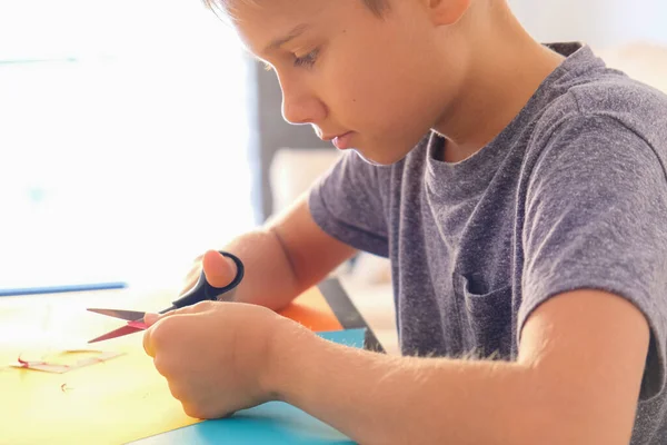 Educação, artesanato de papel para crianças. Criança cortando papel colorido com tesoura e fazendo cartão de saudação em casa — Fotografia de Stock