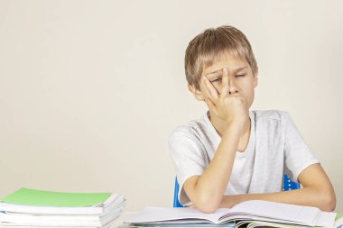Üzgün, üzgün, üzgün okul çocuğu elleriyle yüzünü örterek evde bir yığın okul kitabı ve not defteriyle oturuyor. Eğitim, okul, öğrenme güçlüğü konsepti