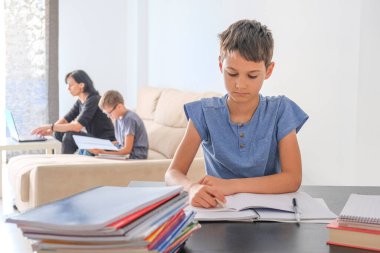 Çevrimiçi öğrenme, uzaktan eğitim, evden internet üzerinden çalışma. Aile evde. Çocuklar ödevlerini kitaplarla, ders kitaplarıyla ve bilgisayarla yapıyor, anneleri çocuklara yardım ediyor, çevrimiçi çalışıyor.