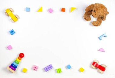 Oyuncak bebek oyuncakları beyaz arka planda oyuncak ayı, ahşap arabalar, oyuncak piramit ve renkli yapı taşlarıyla çerçevelenmiş. Üst manzara, düz uzanma