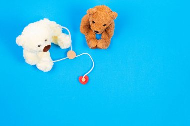 Steteskoplu oyuncak ayı doktor ve oyuncak ayı hasta açık mavi arka planda tahta ilaç aletleriyle