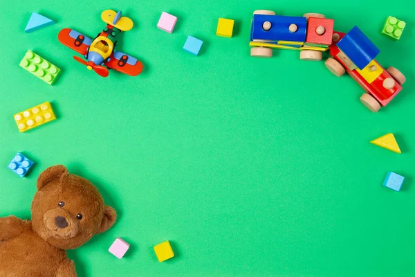 Baby barn pedagogiska leksaker bakgrund. Teddybjörn, trä tåg, röda flygplan och färgglada kuber tegel på ljusgrön bakgrund. Ovanifrån, platt ligg — Stockfoto