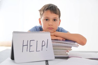 Masada bir sürü kitapla oturan yorgun, hayal kırıklığına uğramış çocuk. Word Help açık deftere yazılmıştır. Ev kavramında öğrenme güçlükleri, okul, eğitim, çevrimiçi öğrenme