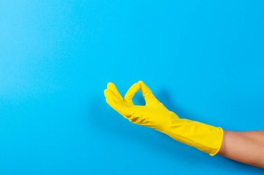 Sarı lastik eldivenli kadın eli bir jest yapıyor. Tamam, mavi arka planda üst manzara.