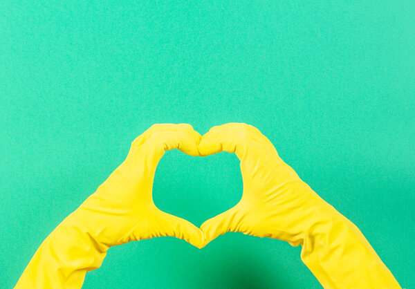 Hands in yellow rubber gloves making heart shape with fingers, on green background