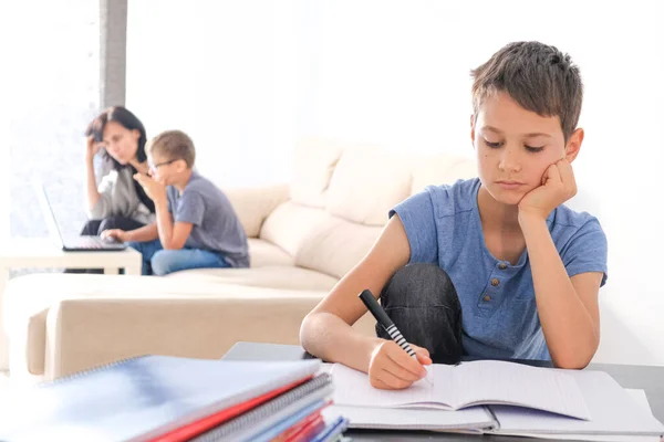 Çevrimiçi öğrenme, uzaktan öğrenme, ev konseptinde kalma. Çocuklar evde ödev yapıyor. Anne, küçük oğluna ödevlerinde yardım ediyor. — Stok fotoğraf