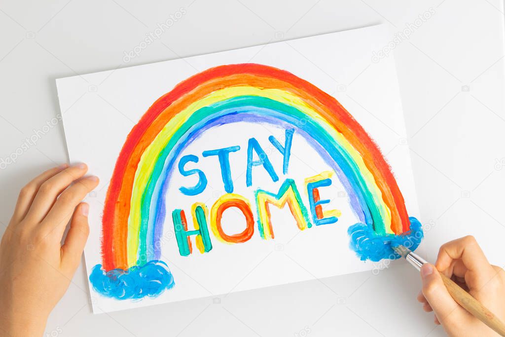 Kid hands painting during quarantine at home. Rainbow with words Stay at home. Social media campaign for coronavirus prevention