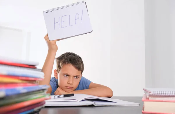 Upset tired preteen child sitting at the table, doing his homework among pile of books. Word Help is written on open notebook — Stock Photo, Image