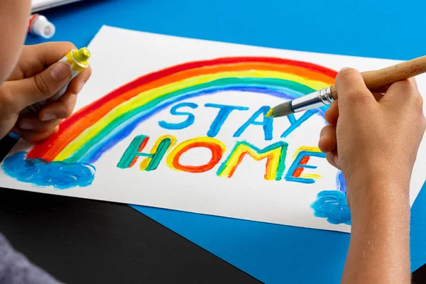 Chico pintando durante la cuarentena en casa. Arco iris con palabras Quédate en casa. Campaña de medios sociales para la prevención del coronavirus — Foto de Stock