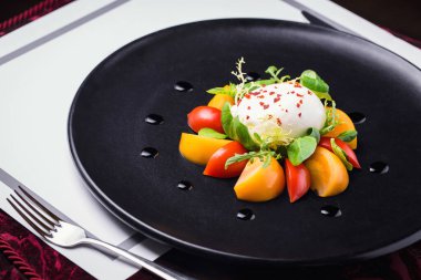Siyah bir tabakta çatallı sebze ve otlarla lezzetli bir buratta restoranı.