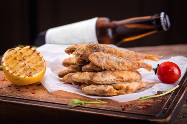 Bira şişesinin arka planında ahşap bir tahtanın üzerinde lezzetli kızarmış kapelinler.