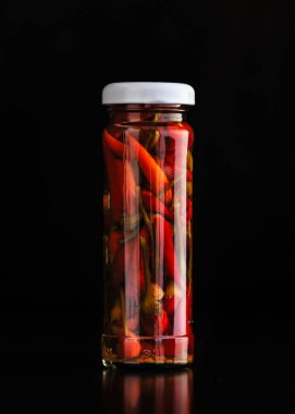 Kavanozda marine edilmiş kırmızı biber. Masanın üzerinde koyu bir arka planda.