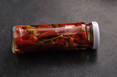 Kavanozda marine edilmiş kırmızı biber. Masanın üzerinde koyu bir arka planda.