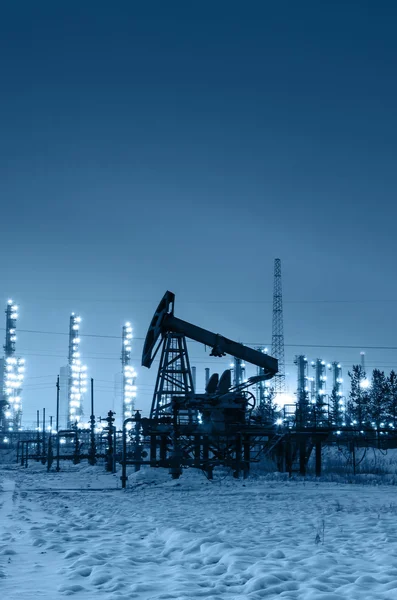 Bomba de aceite y cabeza de pozo en el fondo de la refinería por la noche — Foto de Stock