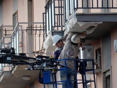 Benevento, Campania, Italya-29 Ekim 2016: iki inşaat işçisi, bir kamyon vinç sepetinin kenarında bir binanın saçak sıvıları sökülürken
