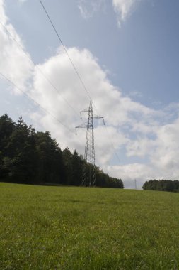 Doğanın ortasında bir elektrik hattı. Şehir binası olan doğa manzarası. Yeşil çimenler ve arkasında mavi gökyüzü olan ağaçlar..