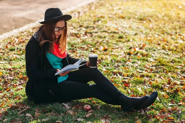 Young woman with book and coffee in park