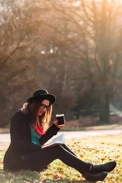 Jeune femme avec livre et café dans le parc — Photo