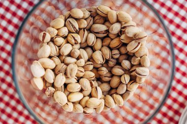 Damalı masa örtüsü üzerine Antep fıstığı ile dolu bir cam kase kadeh Üstten Görünüm