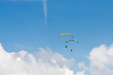 İki kişi mavi gökyüzü altında beyaz bulutlar üzerinde parasailing