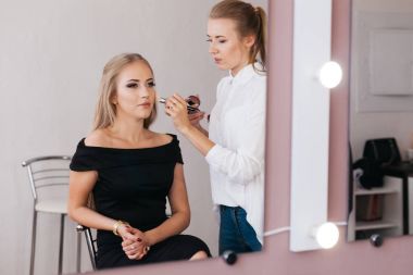 Siyah elbiseli güzel genç kadın ile çalışan profesyonel makyaj sanatçısı