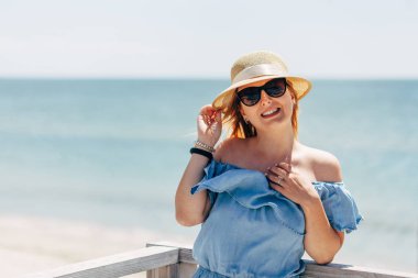 Mutlu bir genç güzel kadın hasır şapkalı ve deniz arka plan mavi elbiseli portre