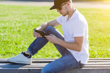 Şehir Park bankta PC tablet açık kullanan genç yetişkin adam. Adam Parkı'nda okuma.