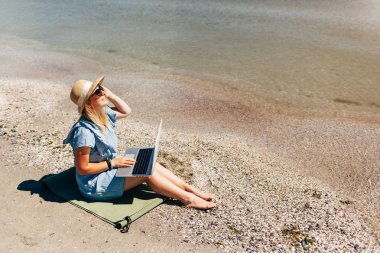 Young beautiful woman sitting with laptop on the beach near the sea clipart
