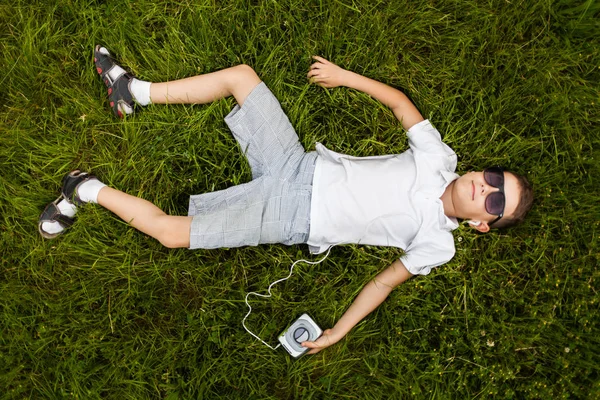 Little boy in sunglasses lying on ground and listening to music in earphones