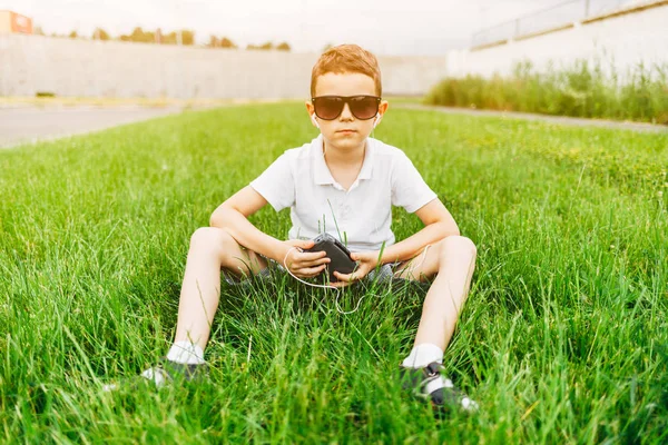 Mały Chłopiec Okulary Siedząc Trawie Słuchanie Muzyki Słuchawkach — Zdjęcie stockowe