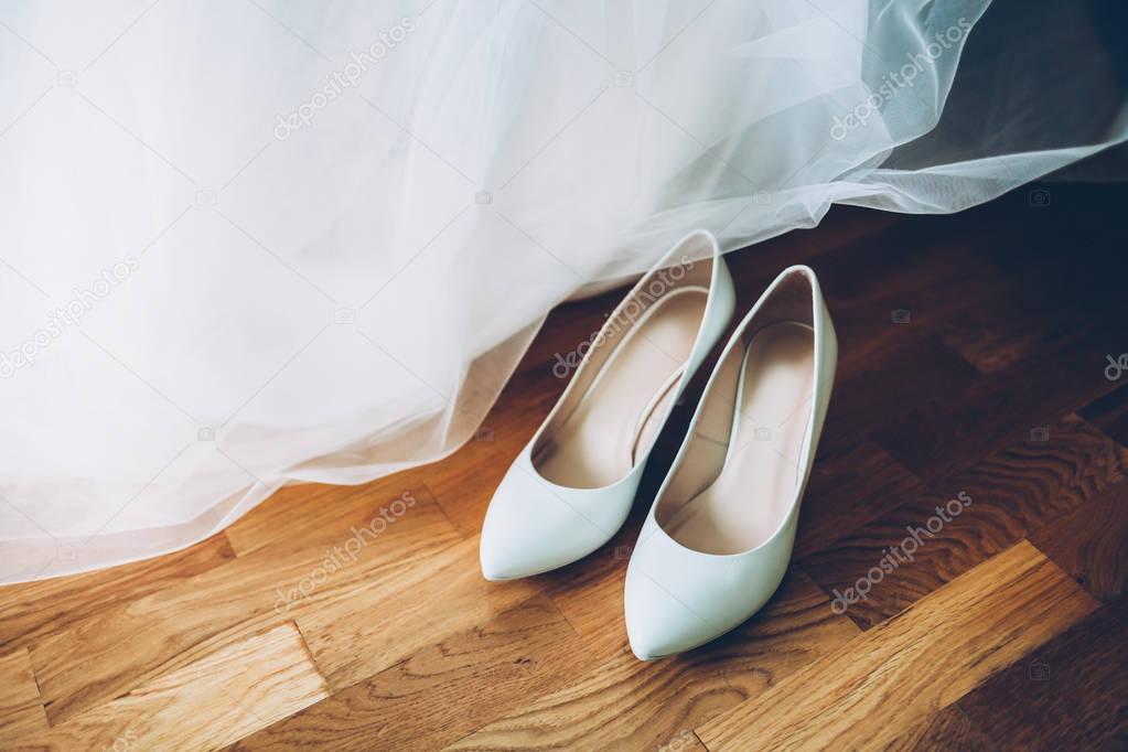White women's wedding shoes on a background of wooden floors, along with a wedding dress. Wedding concept