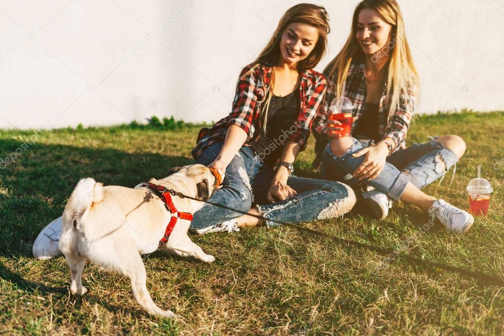 twin sisters hanging out together in a park with a cute pug dog