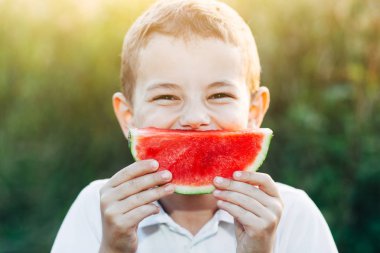 Küçük çocuk beyaz t-shirt holding dilim taze kırmızı karpuzun içinde closeup portresi