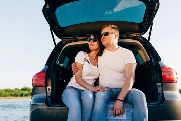 Веселая пара сидит в машине открытый багажник и смотреть карту, дорожная концепция поездки — стоковое фото