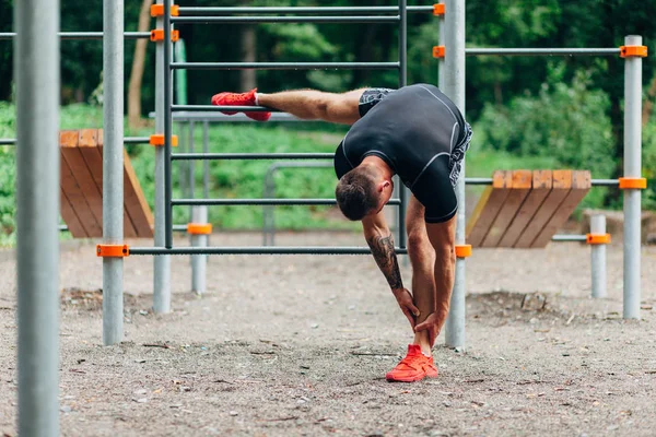 Joven atleta caucásico en ropa deportiva negra y tatuajes, entrenamiento al aire libre y posando — Foto de Stock