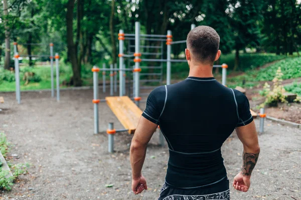 Jovem atleta caucasiano em sportwear preto e tatuagens, treinando ao ar livre e posando — Fotografia de Stock