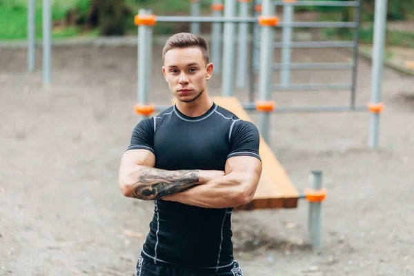 Jovem atleta caucasiano em sportwear preto e tatuagens, treinando ao ar livre e posando — Fotografia de Stock